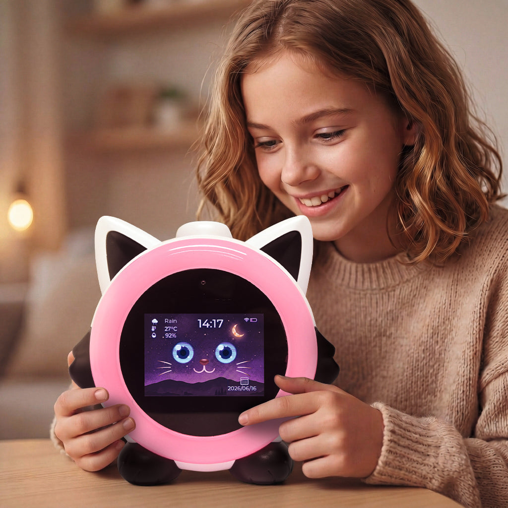 A smiling young girl with wavy light brown hair holds a pink cat-shaped smart alarm clock in a cozy, warmly lit room. The clock features black cat ears, a pink outer frame, and a central screen displaying a cartoon cat face and the time 14:17.